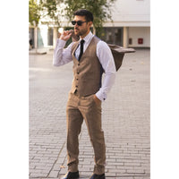 Vyras, vilkintis rudą kostiumą, su akiniais nuo saulės ir kuprine miesto gatvėje.